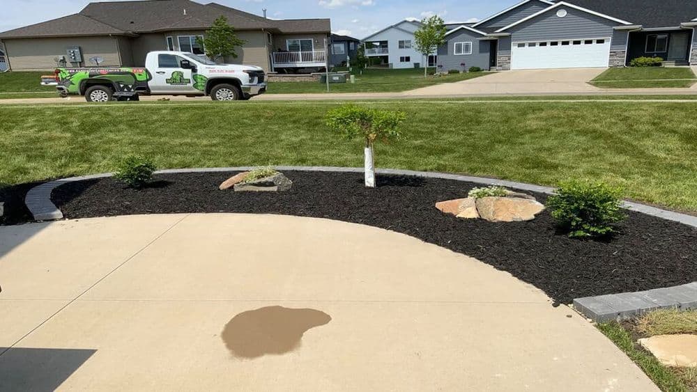 Landscaped yard with mulch, rocks, and a view of houses and a service truck in the background.