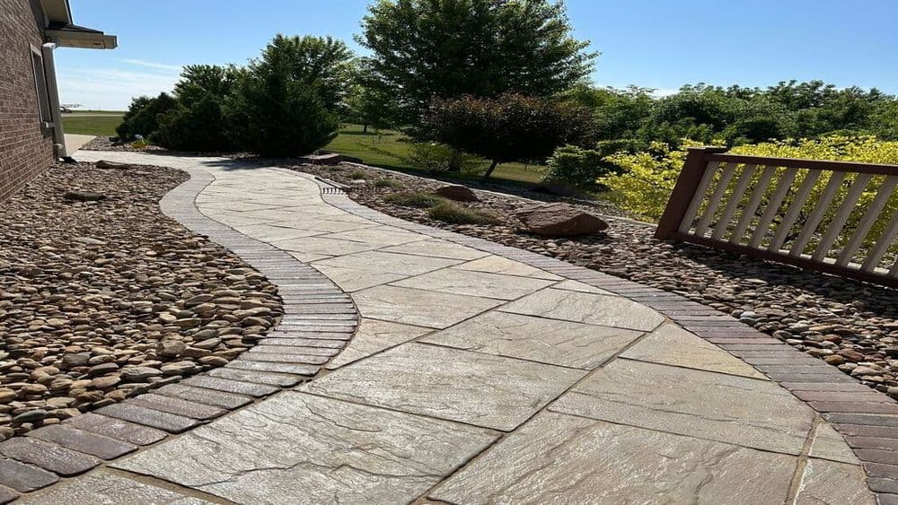 Curved stone walkway with pebbles and greenery, leading to a bright outdoor space.