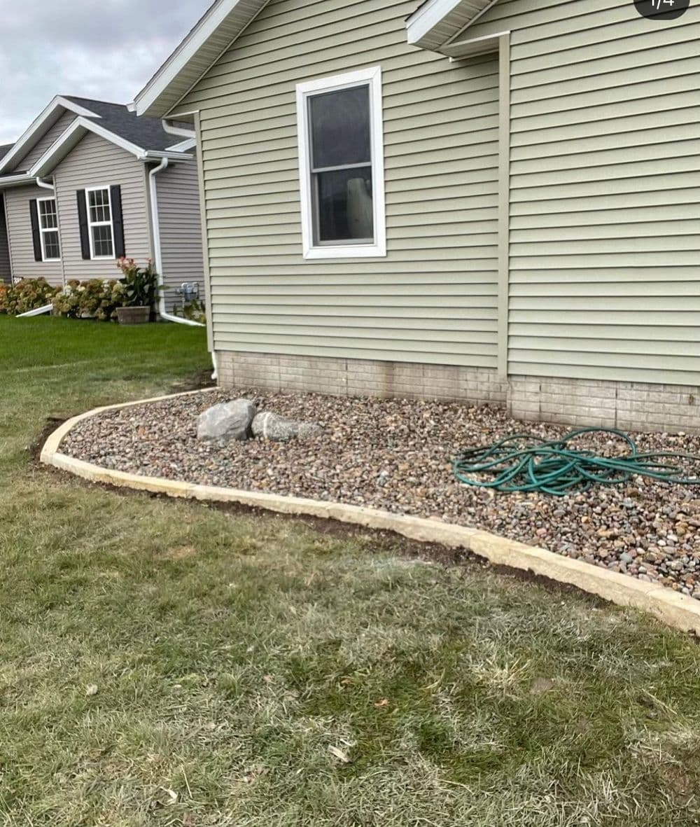 Side view of a house with gravel landscaping, bordered by stone edging and garden hose.
