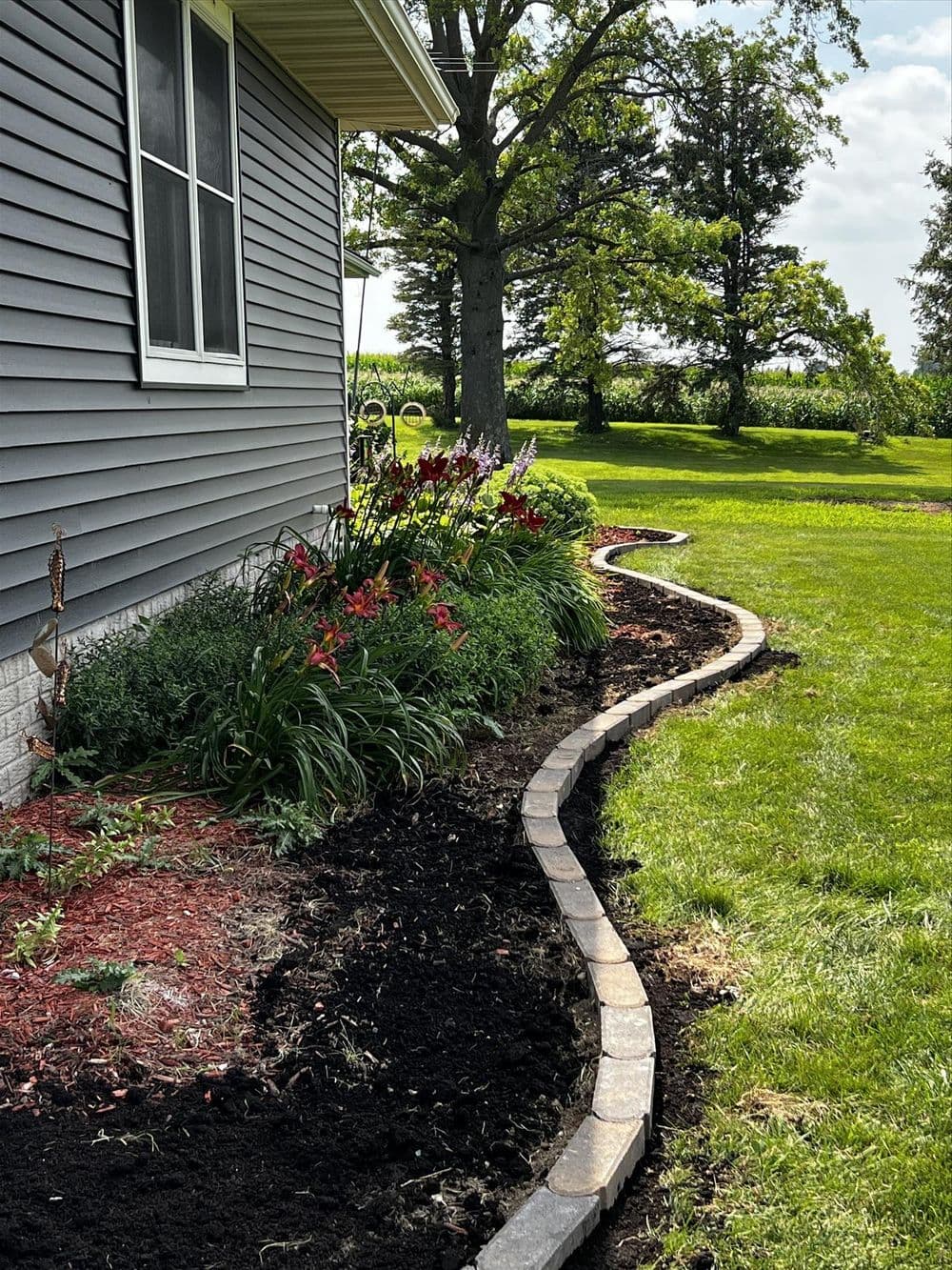 Curved garden bed featuring colorful flowers and fresh mulch beside a gray house.