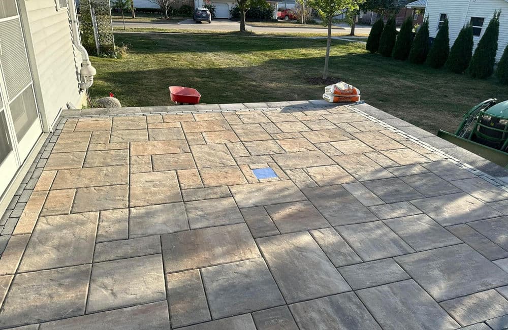 Newly installed patio with textured pavers, grass yard, and landscaping in background.