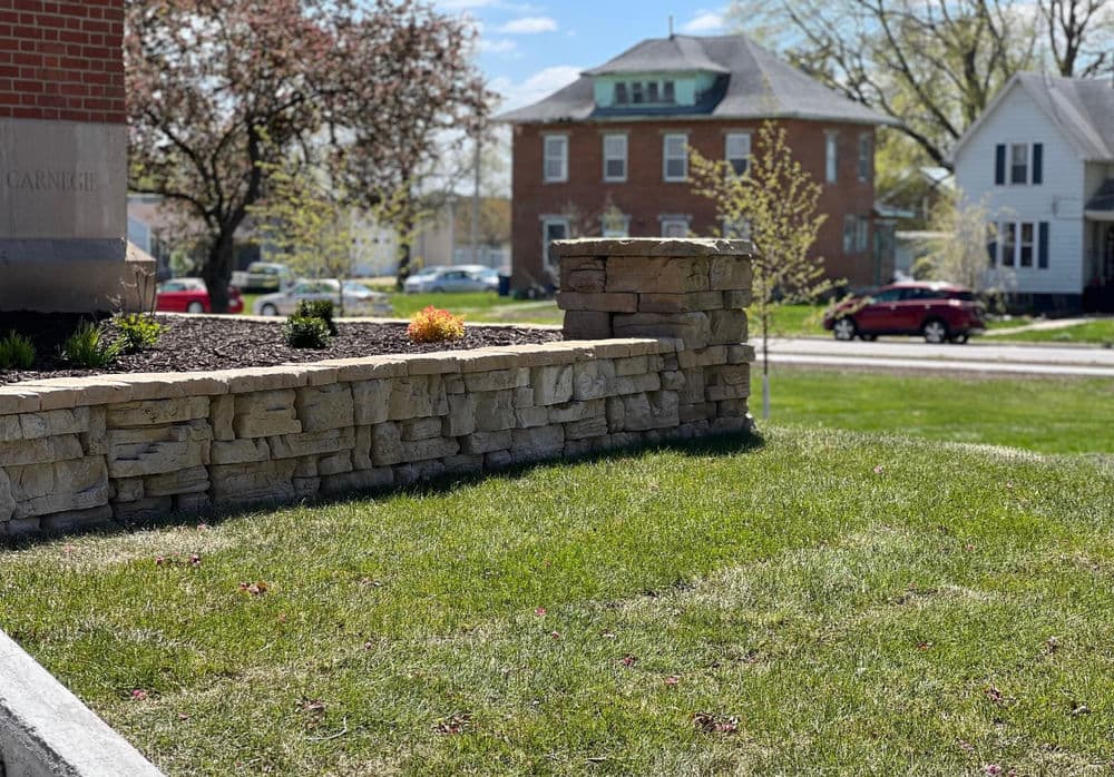 Stone retaining wall with landscaped grass area in front of a residential neighborhood.