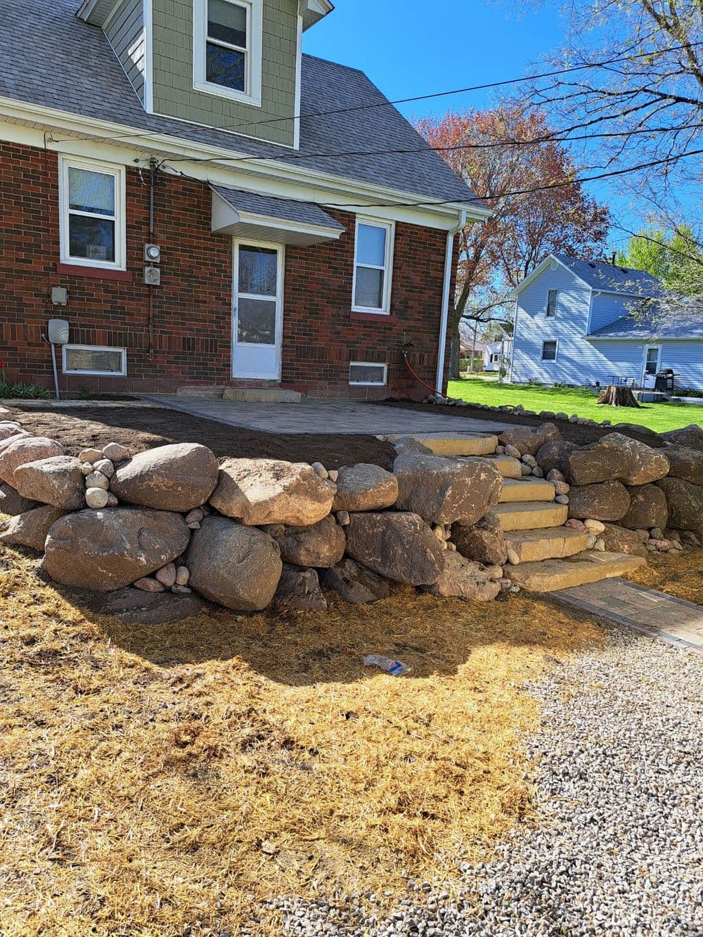 Stone terraced landscaping with steps leading to a brick house and green lawn.