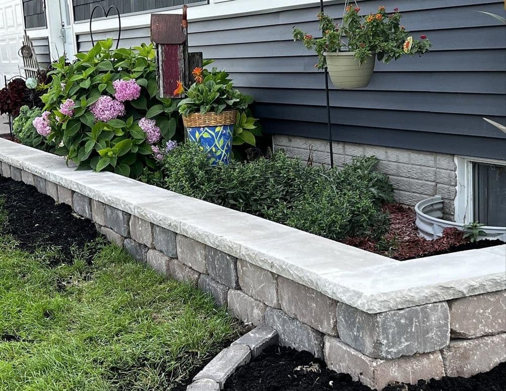 Landscaped garden featuring a stone wall, colorful floral arrangements, and lush greenery.