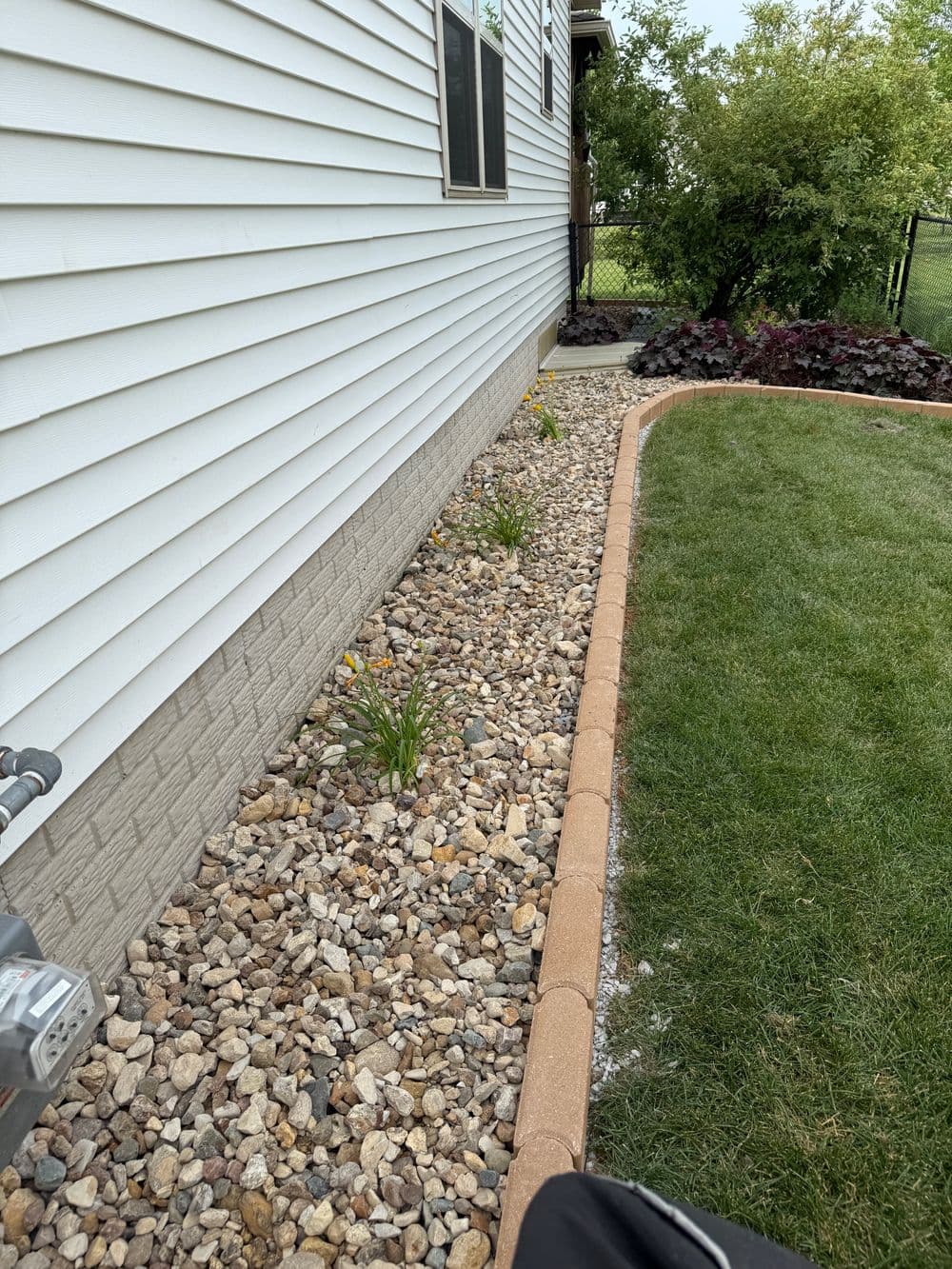 Landscaped side yard with gravel, edging, and flowering plants near a house.