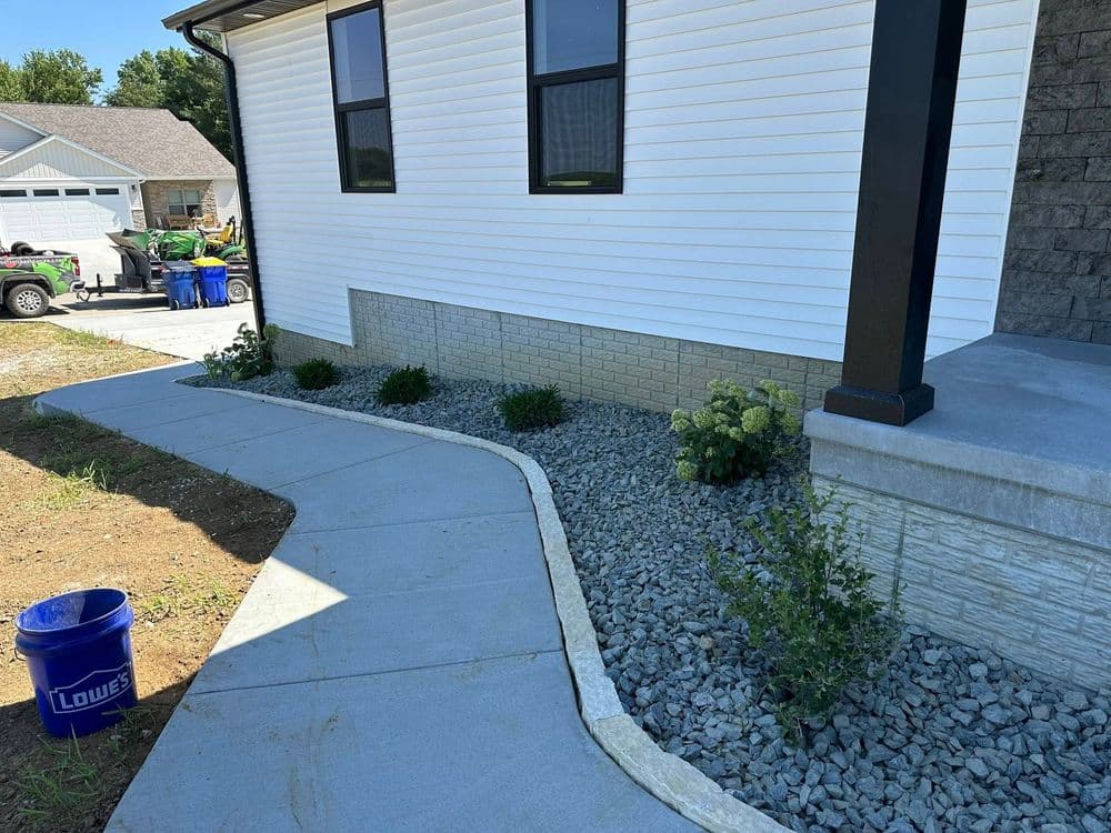 Landscape design featuring a curved concrete walkway, gravel border, and low maintenance plants.