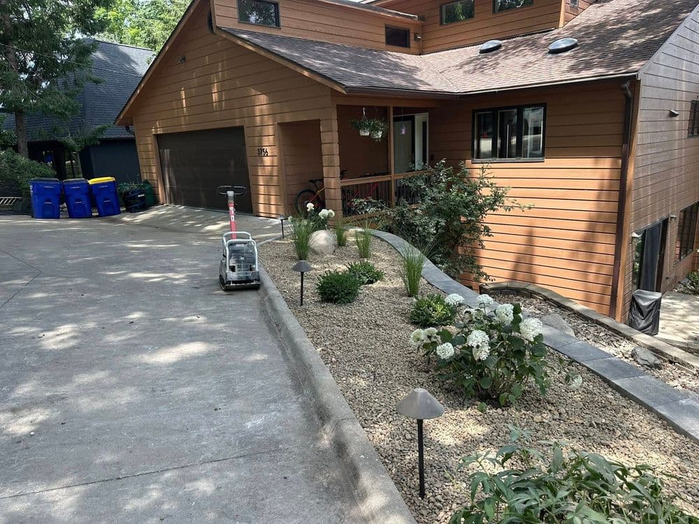 Modern home with landscaped driveway, flower beds, and recycling bins.