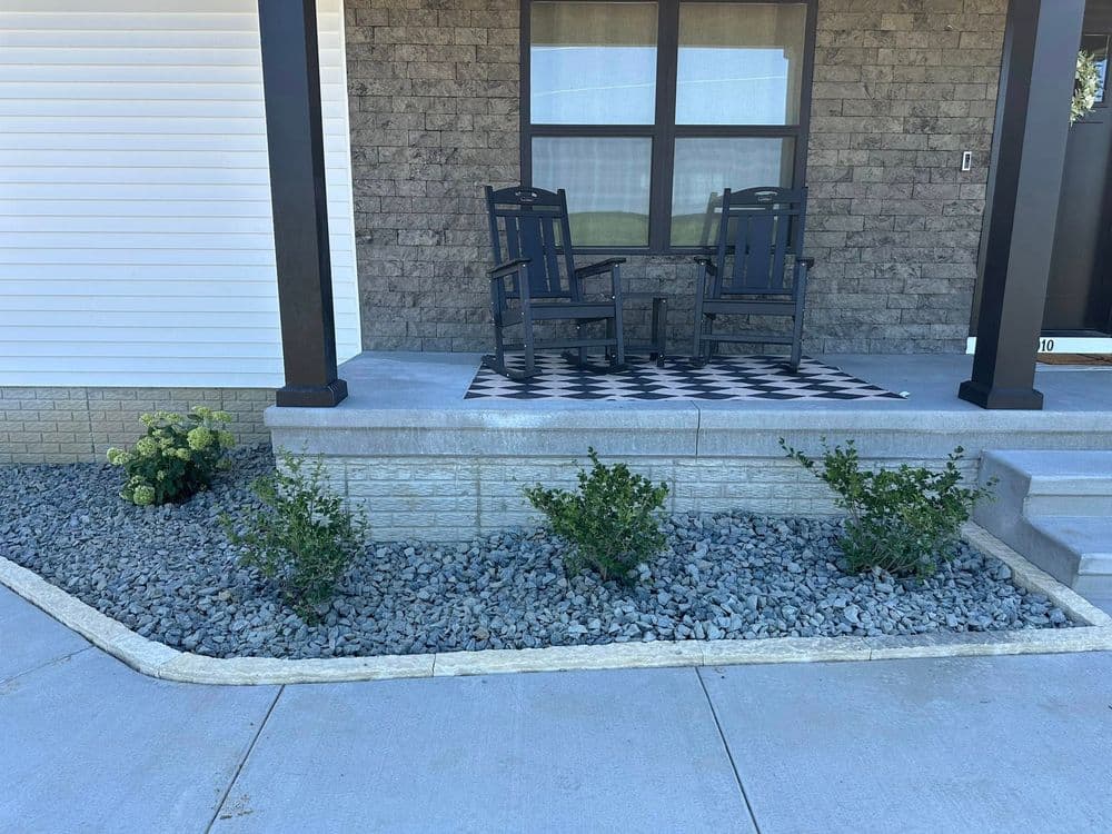 Charming front porch with black chairs, checkered rug, and landscaped stone garden.