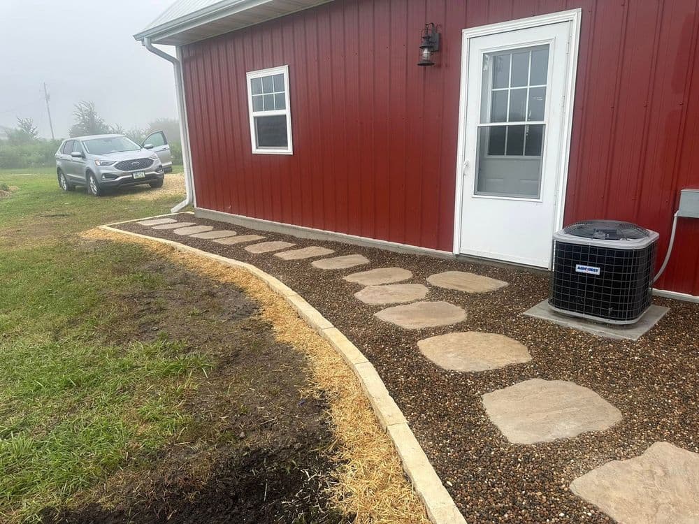 Pathway of stepping stones leading to a door on a red barn, with a car parked nearby.