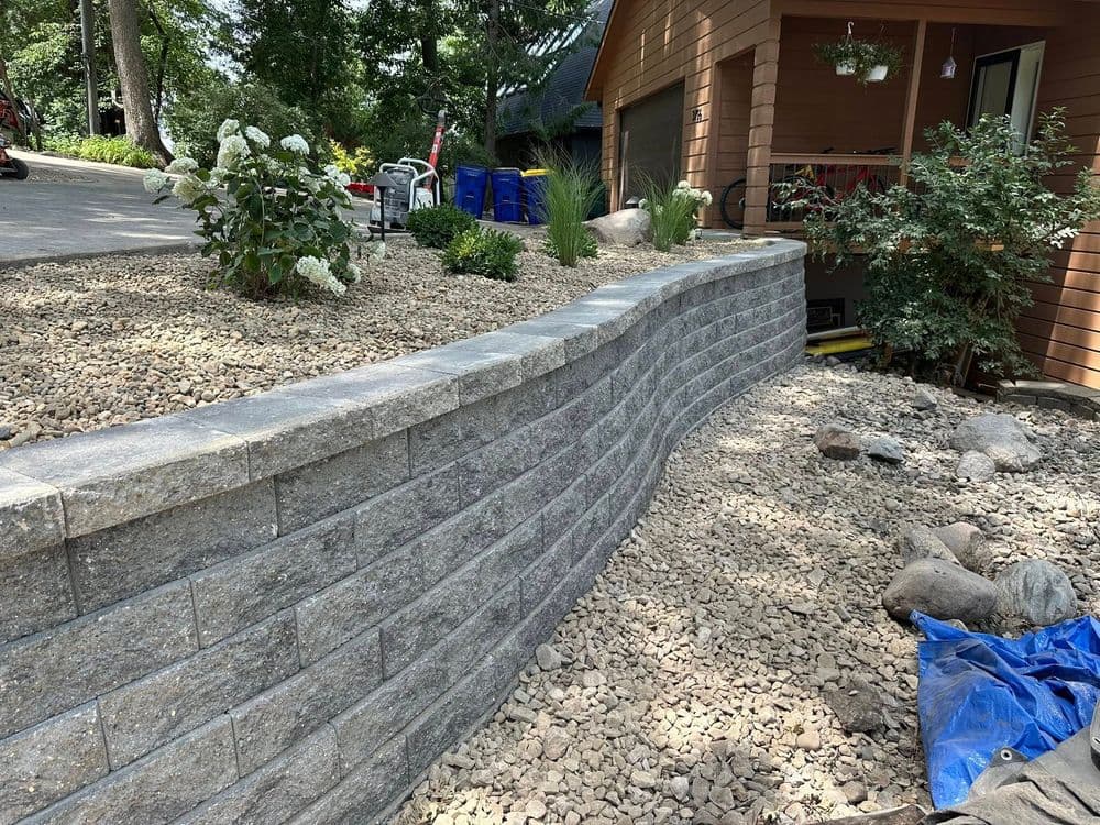 Landscape design featuring a curved gray stone retaining wall with gravel and plants.
