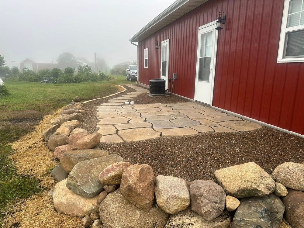 Stone pathway and gravel landscaping beside a red barn-style house in foggy weather.