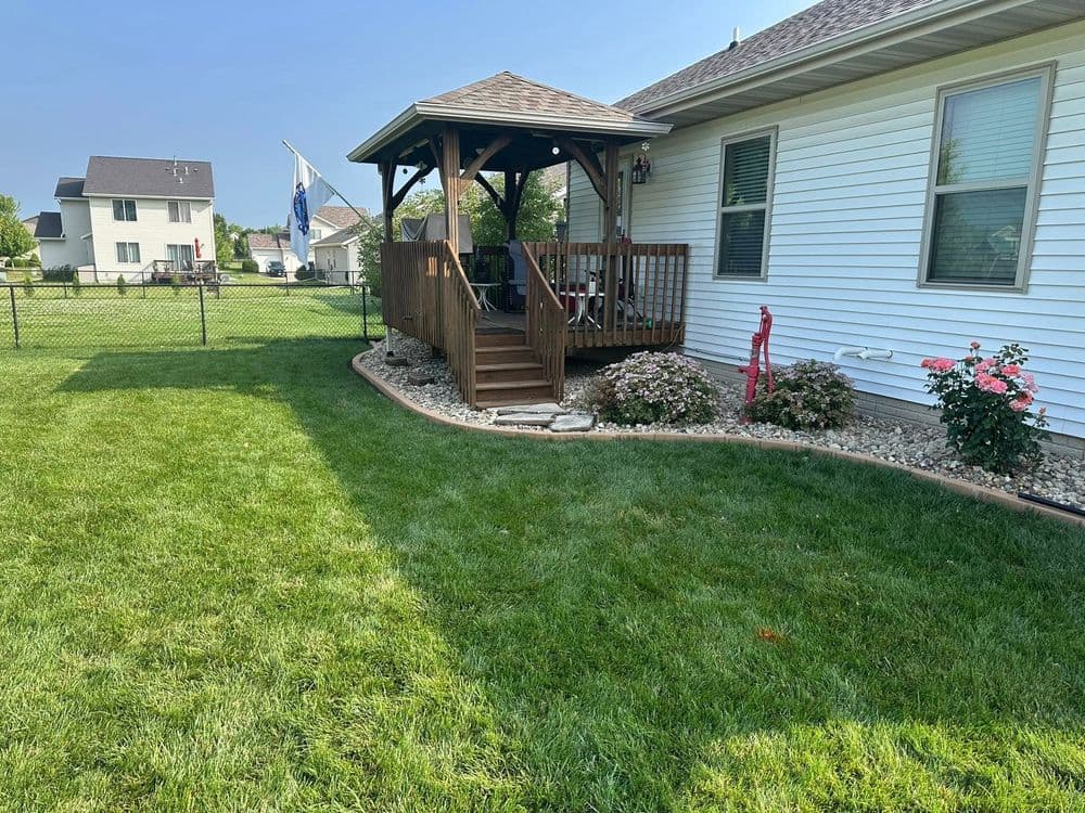 Wooden gazebo in a well-maintained backyard with green lawn and landscaping features.