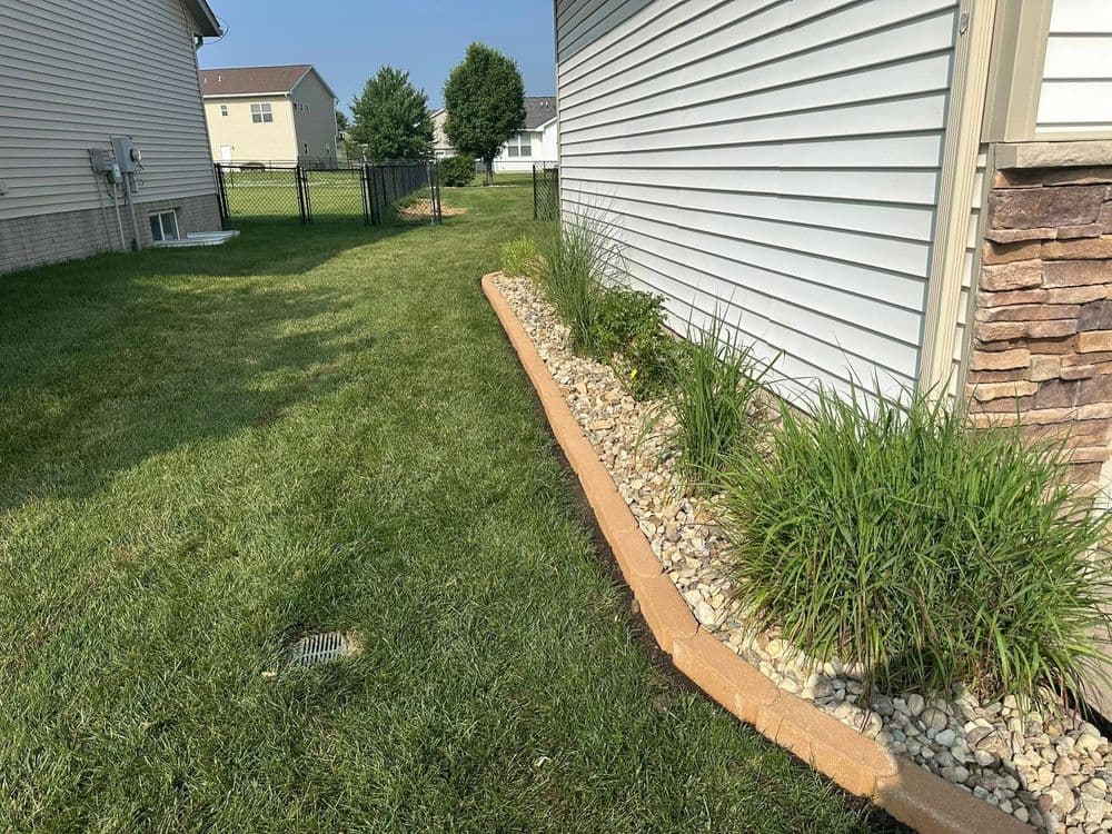 Landscaped side yard featuring a gravel border, plants, and grass near residential homes.
