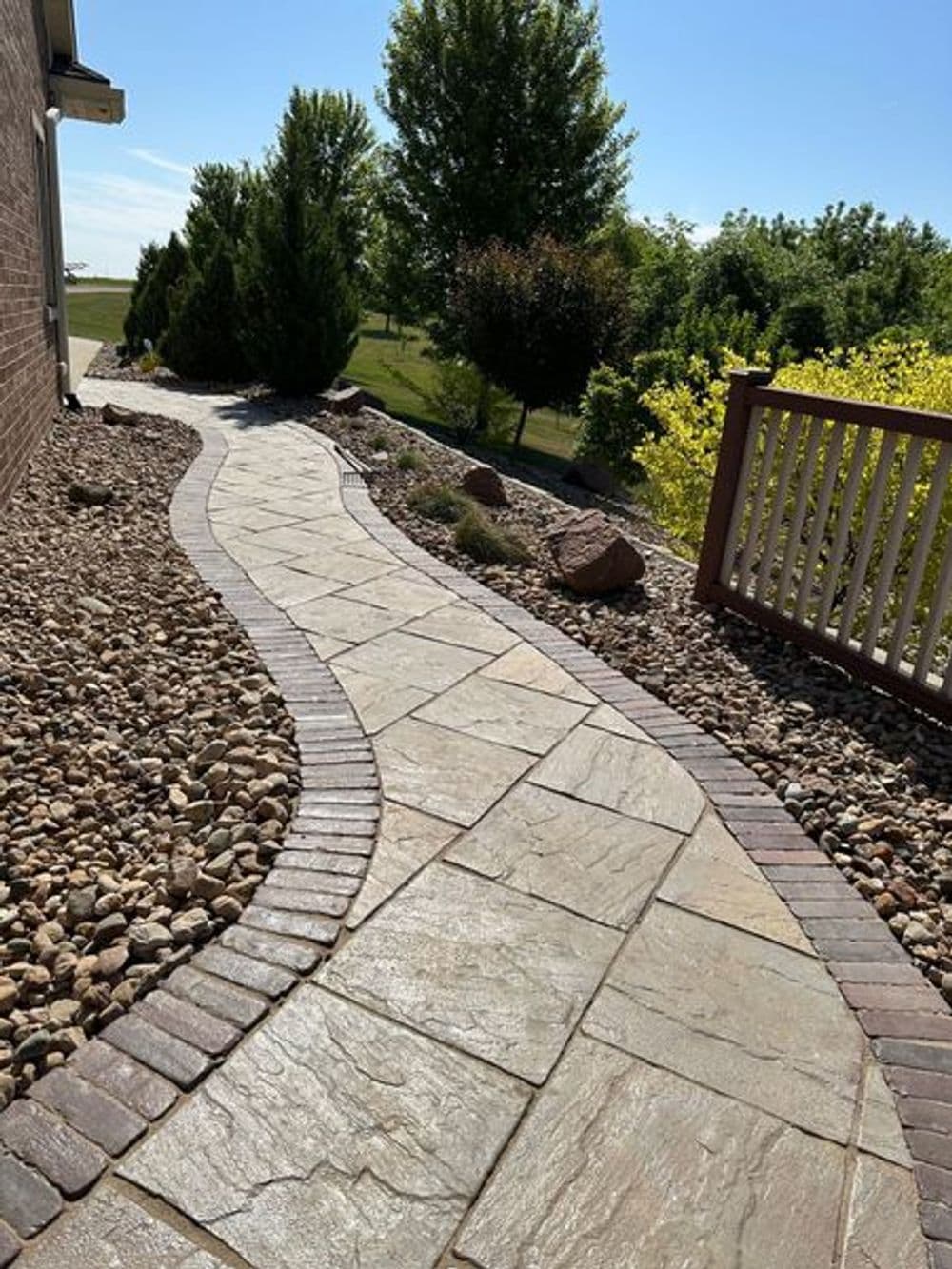 Curved stone pathway lined with gravel and shrubs, leading through a sunny garden.