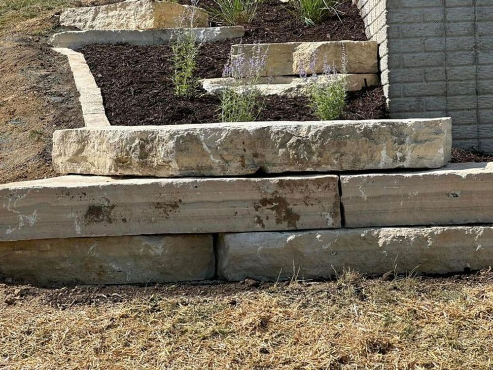 Stacked stone retaining wall with purple flowers and mulch in a landscaped garden.