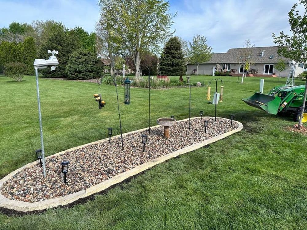 Landscape design featuring a stone garden bed with bird feeders and outdoor lighting in a green yard.