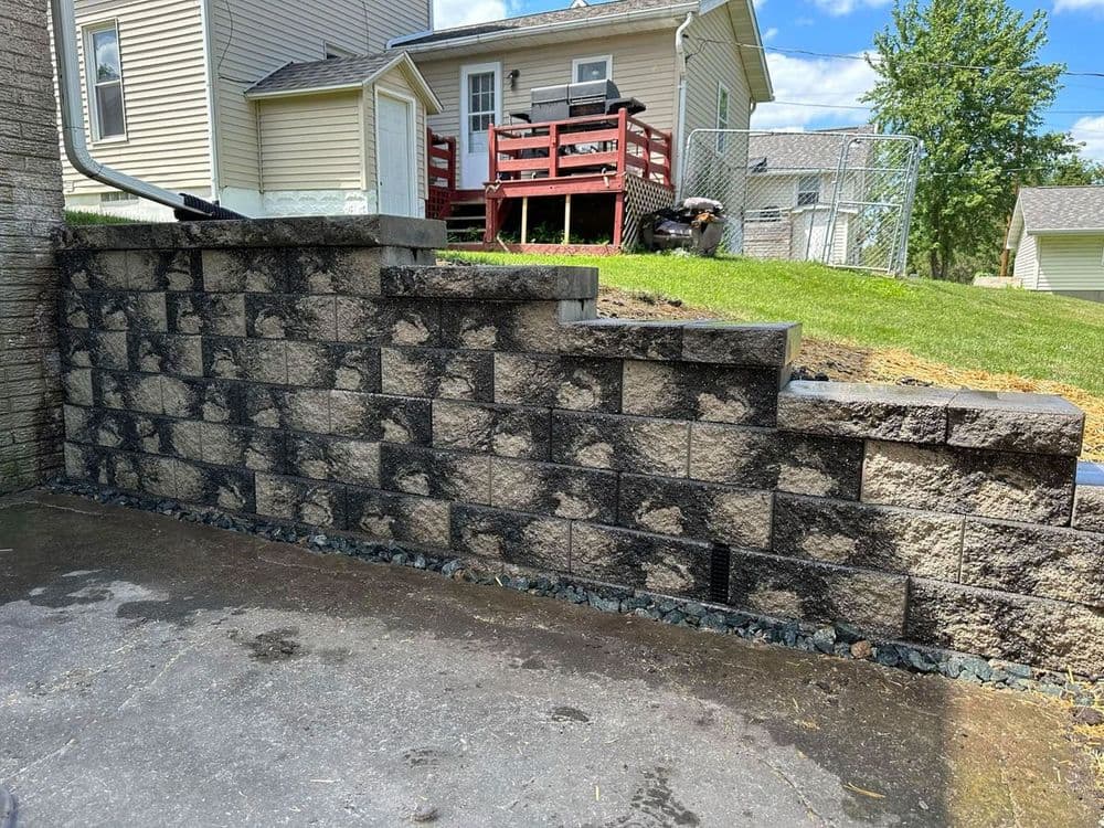 Retaining wall made of stone blocks with landscaped yard and house in the background.