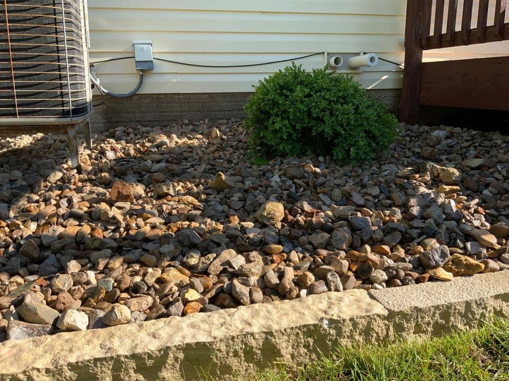 Rocky landscape featuring a bush near an air conditioning unit and wooden deck.