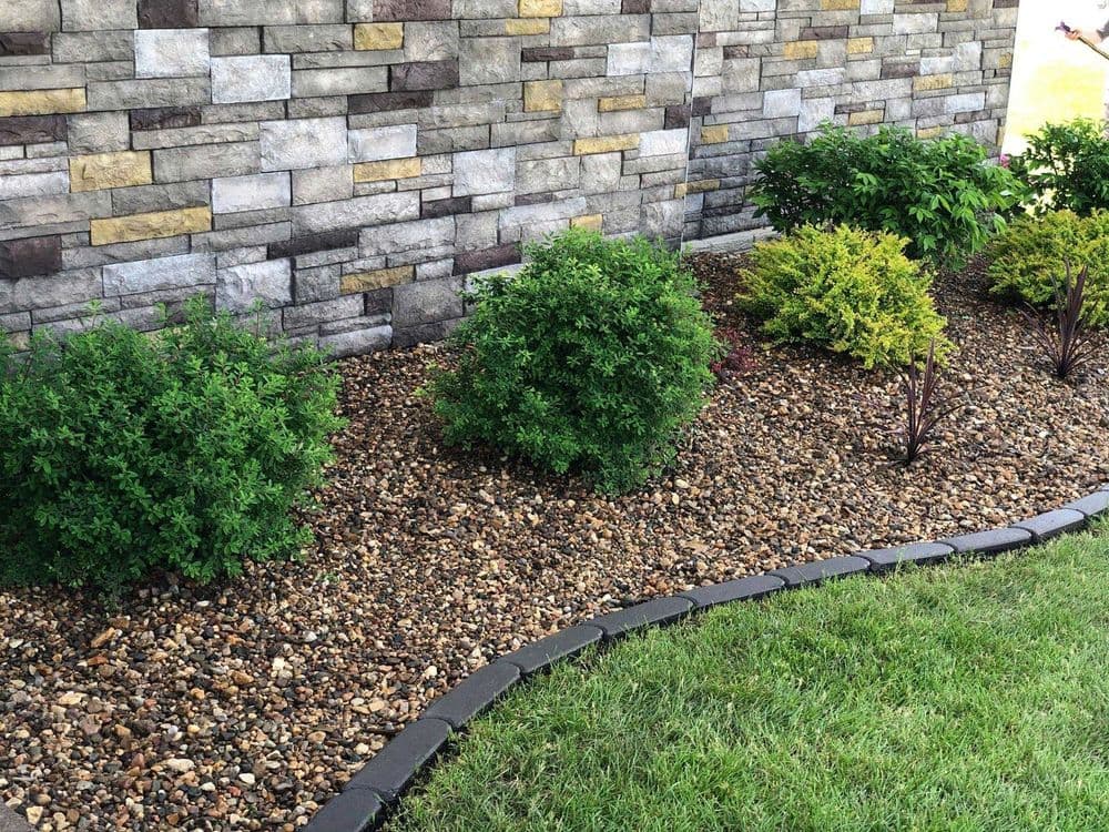 Lush garden shrubs against a stone wall with decorative gravel landscaping.